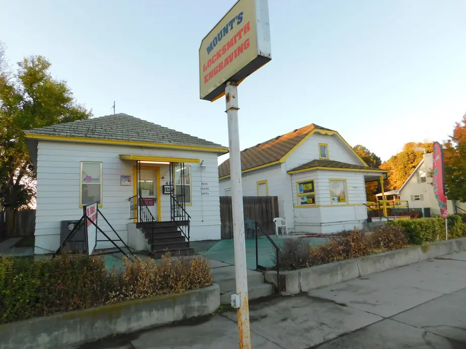 Mount's Lock & Key storefront at golden hour, white clapboard with yellow trim under the MOUNT'S LOCKSMITH ENGRAVING pole sign